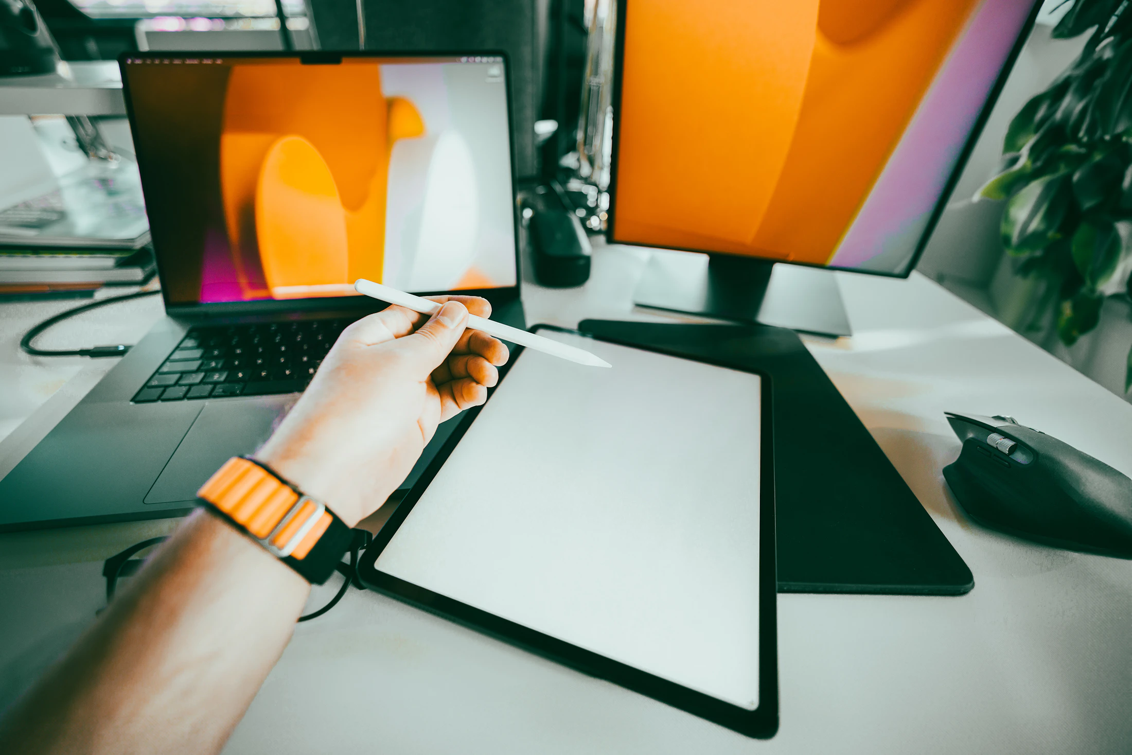 A bright creative workspace with a laptop, drawing tablet, stylus, and large display